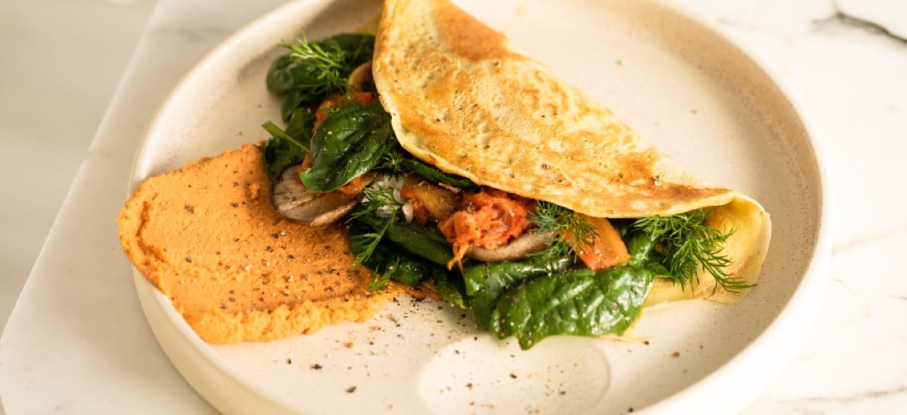 A folded omelet on a white plate filled with green spinach and a beige chickpea spread.